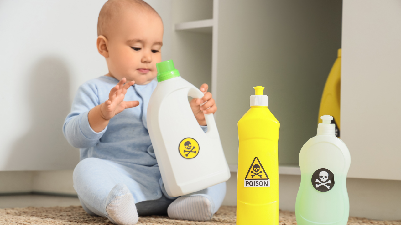 A baby reaching for household cleaning bottles marked with poison warnings