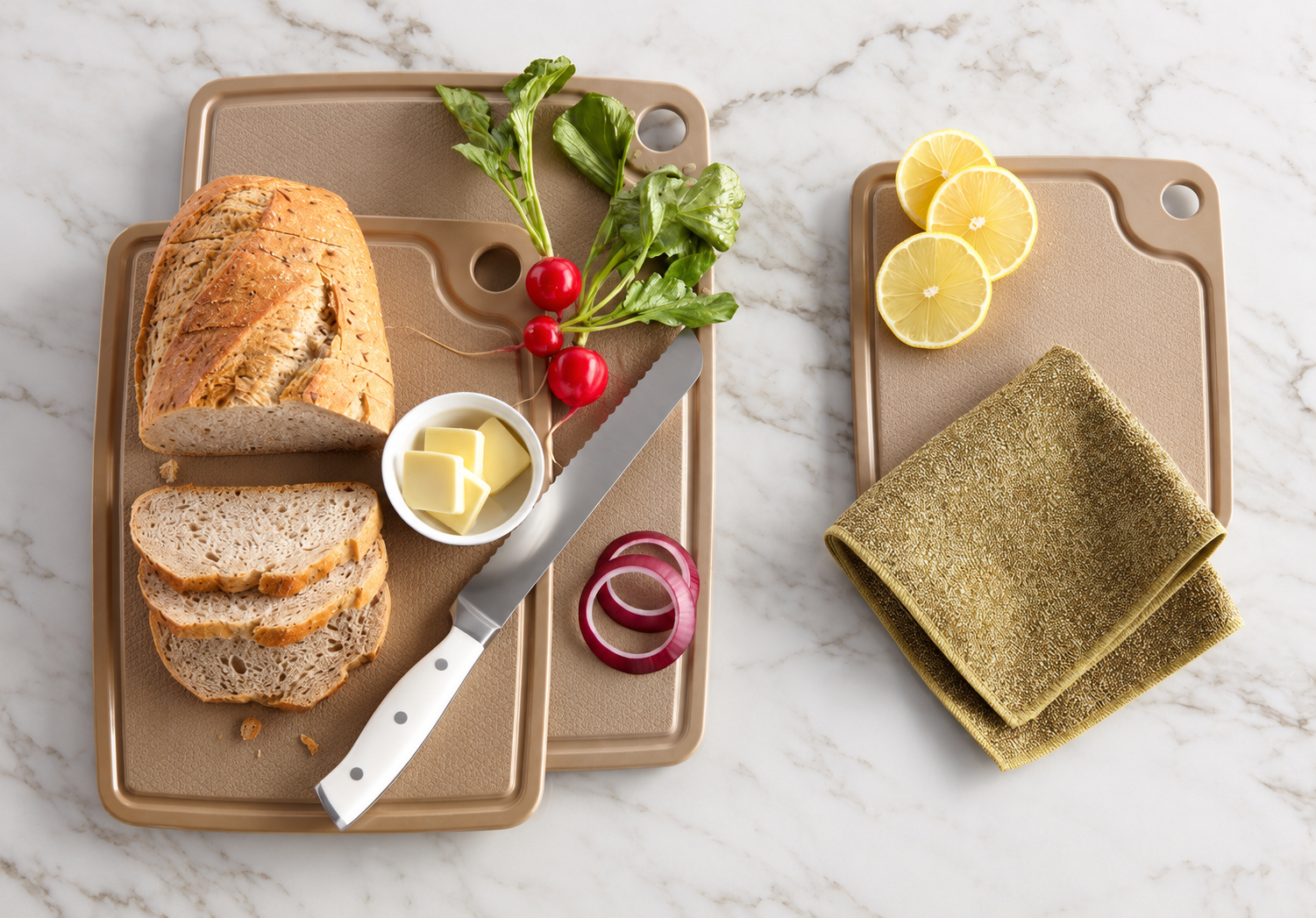 Three Norwex cutting boards on a marble counter with bread, vegetables, lemons, a knife, and a kitchen cloth.